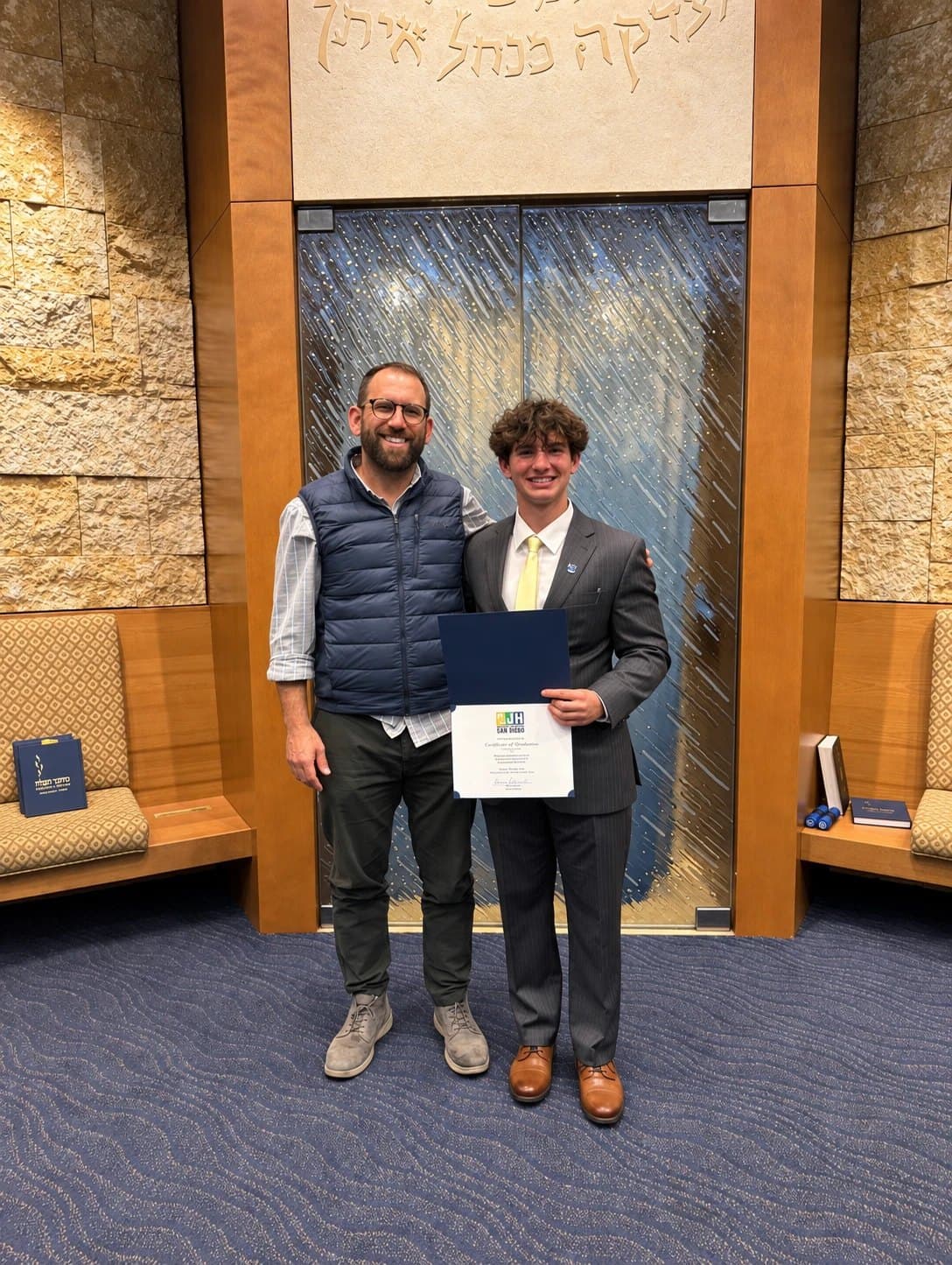 Maxwell Keller holding his Community Jewish High certificate of graduation beside Rabbi Hanan Lieberman at Temple Emanu-El in San Diego