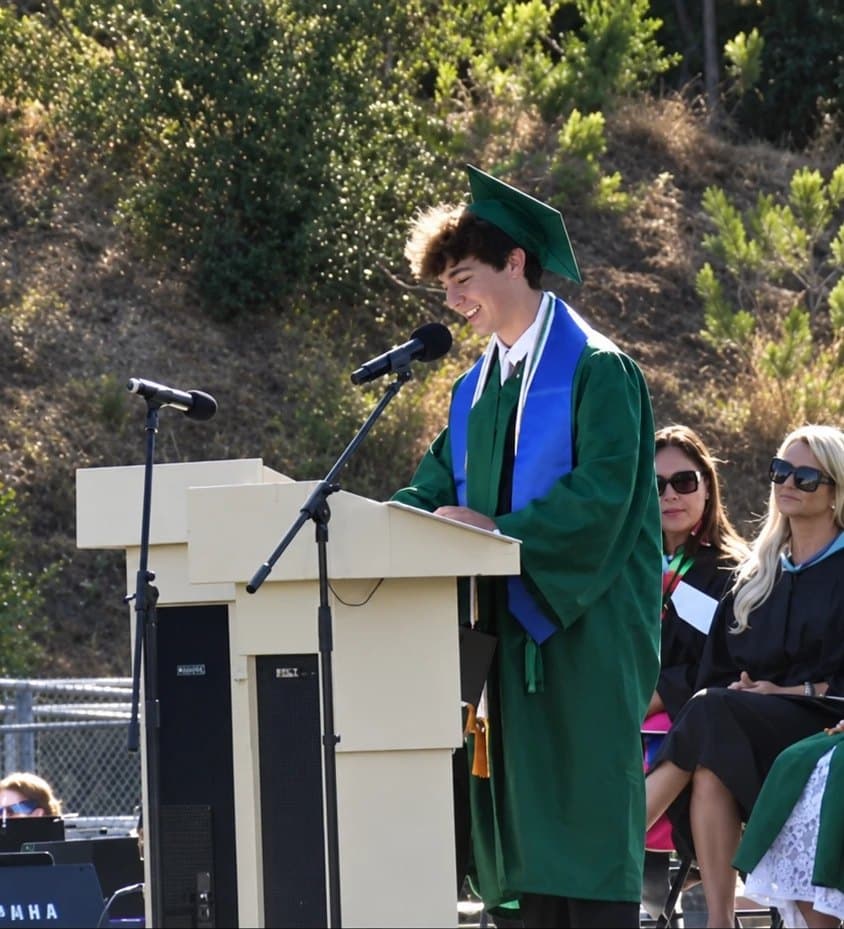 Maxwell Keller in a green cap and gown giving the valedictorian speech at the Patrick Henry High School 2026 commencement